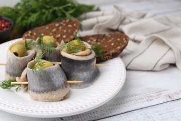 Delicious herring rolls with olives, dill and bread on white wooden table, closeup. Space for text