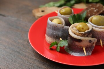 Delicious herring rolls with olives and parsley on wooden table, closeup. Space for text