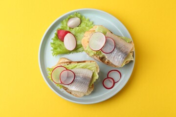 Tasty sandwiches with herring, radish and lettuce on yellow background, top view