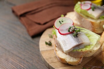 Tasty sandwiches with herring, radish and lettuce on wooden table, closeup. Space for text