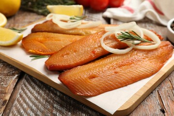 Delicious smoked herring fillets with lemon slices, onions and rosemary on wooden table, closeup