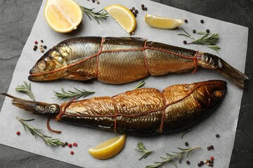 Delicious smoked herrings with lemon slices, peppercorns and rosemary on black table, top view