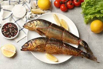 Delicious smoked herrings with lemon slices and other products on grey table, flat lay