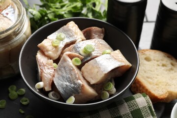 Pieces of delicious herring with green onions on black table, closeup