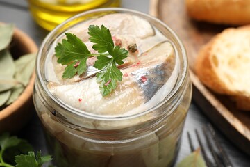 Pieces of delicious herring with spices and parsley in jar on black table, closeup