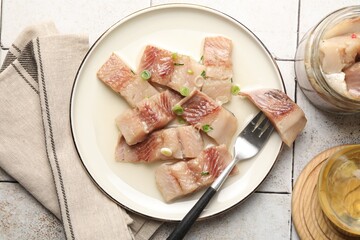 Pieces of delicious herring with green onions on tiled table, flat lay