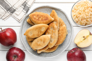 Delicious fried pyrizhky (stuffed pies) and apples on white wooden table, flat lay