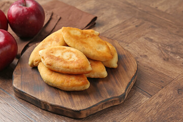 Delicious fried pyrizhky (stuffed pies) and apples on wooden table, closeup. Space for text