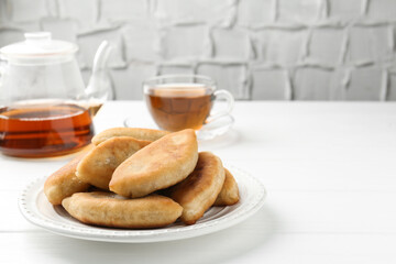 Delicious fried pyrizhky (stuffed pies) and tea on white wooden table, closeup. Space for text