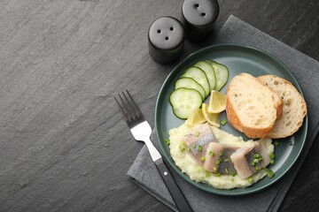 Pieces of delicious herring, mashed potato, cucumber slices and bread served on black table, flat lay. Space for text