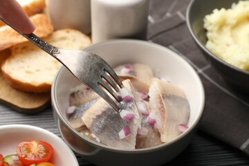 Eating delicious herring with onions at black table, closeup
