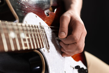 Man playing guitar with mediator on black background, closeup