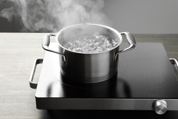 Cooking pot with boiling water and stove on wooden table against grey background, closeup