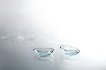 Pair of contact lenses and water drops on light mirror surface, closeup