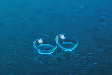 Pair of contact lenses and water drops on blue mirror surface, closeup