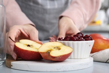 Woman with apples and cherries at light grey table, closeup