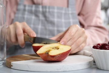 Woman cutting apples at light grey table, closeup