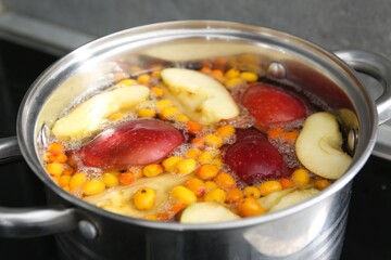 Making compot of apples and sea buckthorn berries. Simmering fruits in pot on stove, closeup
