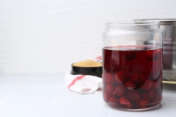 Tasty cherry compot in glass jar on white tiled table, closeup. Space for text
