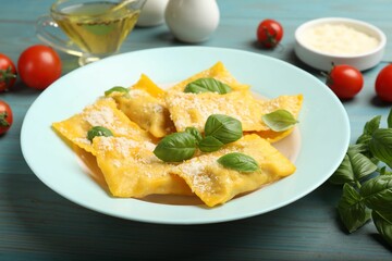 Delicious ravioli with cheese and basil served on light blue wooden table, closeup