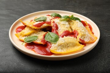 Delicious ravioli with tomato sauce, parmesan cheese and basil on black table, closeup