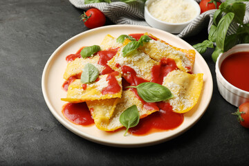 Delicious ravioli with tomato sauce, parmesan cheese and basil on black table, closeup