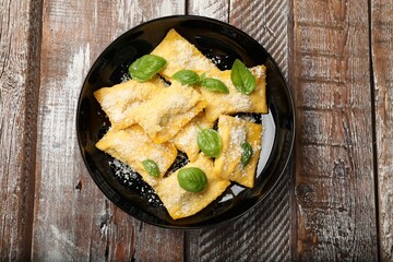 Delicious ravioli with parmesan cheese and basil on wooden table, top view