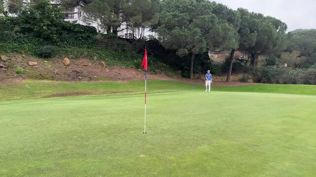 A golfer putts from the edge of the green, misjudging both direction and strength, as the ball veers away from the hole under cloudy skies.

