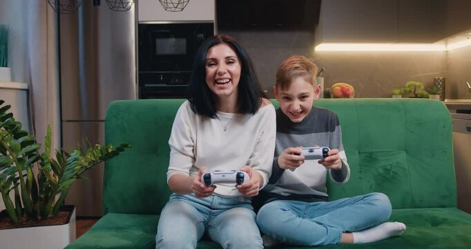Family celebrating victory in video game and gives five. Entertainment and modern lifestyle concept. Mother and son playing video game using controllers when they spend joint leisure at home.