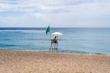 A solitary figure vigilantly surveys the tranquil waters from an elevated chair on a peaceful beach