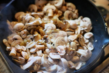 A hot pan filled with freshly sliced mushrooms and onions being sauteed. The steam rising from the ingredients highlights the savory aroma and deliciousness of this simple homemade dish.