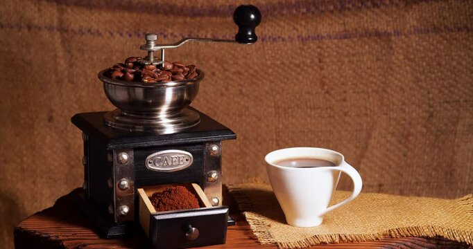 Fried Coffee Beans in a Manual Grinder. Preparation of Fresh Beverage Morning Coffee for Breakfast with Rotating Effect. Mill for Grinding with Cup and Bag with Coffee