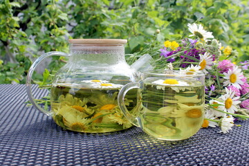 There is a glass teapot with chamomile tea and a cup on the table.	