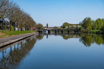 Boats and houses reflecting in the water of the river Lys or Leie in Menen, West Flanders, Belgium