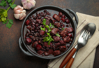 Brazilian feijoada, a hearty stew of black beans, various cuts of meat, and sausage, garnished with...
