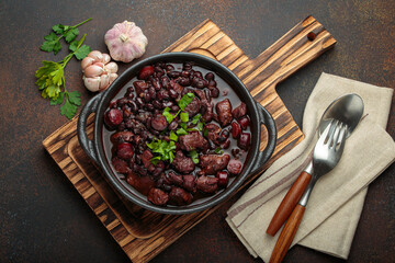 Brazilian feijoada, a hearty stew of black beans, various cuts of meat, and sausage, garnished with...