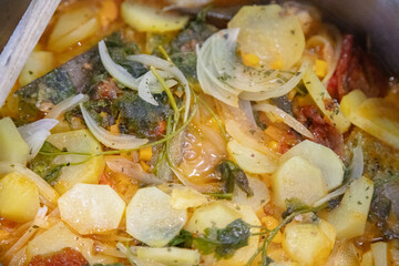 Traditional Portuguese codfish stew, known as caldeirada de bacalhau, prepared in a stainless steel pot with sliced potatoes, onions, tomatoes, peppers, herbs and olive oil.Homemade meal on a stovetop