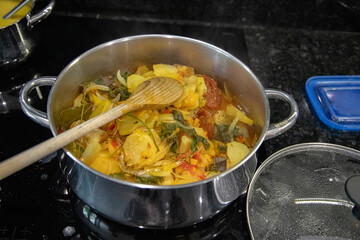 Traditional Portuguese codfish stew, known as caldeirada de bacalhau, prepared in a stainless steel pot with sliced potatoes, onions, tomatoes, peppers, herbs and olive oil.Homemade meal on a stovetop