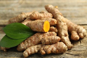Pile of tumeric rhizomes with leaves on wooden table, closeup