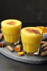Delicious turmeric latte, powder and rhizomes on black wooden table, closeup
