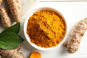 Aromatic turmeric powder, fresh roots and leaves on white wooden table, flat lay