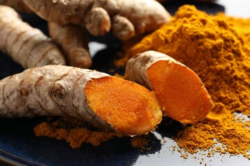 Aromatic turmeric powder and fresh roots on blue plate, closeup