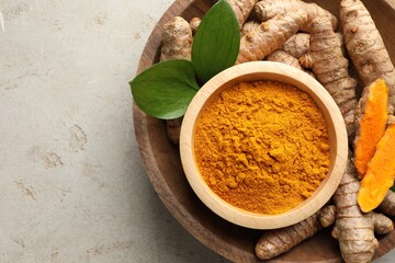Aromatic turmeric powder in bowl, fresh roots and leaves on light grey table, top view. Space for...