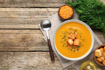 Delicious lentil cream soup served on wooden table, flat lay. Space for text