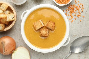 Delicious lentil cream soup served with croutons on light grey table, flat lay