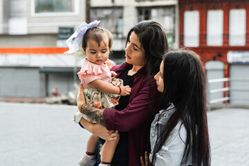 young latina mother holding her young daughter while looking at her with her partner next to her, sad little girl