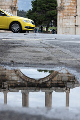 Reflection of a part of Hadrian's Arch in water on asphalt, Athens.