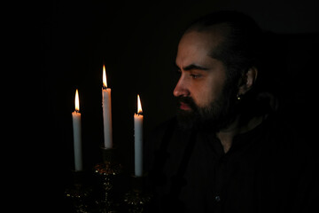 A man thoughtfully gazes at three lit candles, creating a serene and introspective atmosphere. The...