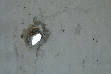 A concrete wall features a large hole revealing a brighter area behind it. The rough surface shows...