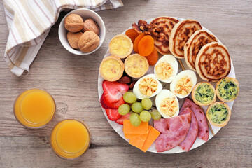 Breakfast or brunch grazing board. Assortment of items including fruit, ham, quiche, pancakes and eggs. Above view table scene on a wood background.